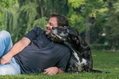 Liegender Martin Rütter, der von einem liegenden Hund geküsst wird
